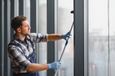 Modern bir ofis binasının camını silmek için cam temizleyicisi eldiven takıyor.