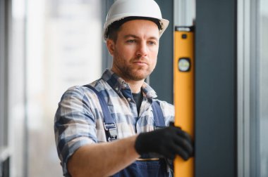 İnşaat aşamasında binanın içine pencere çerçevesi yerleştirilirken koruyucu kask ve eldiven takan kişi ruh seviyesini kullanıyor