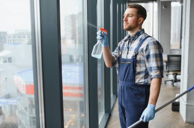 Temizlik işçisi büyük bir ofis penceresine deterjan püskürtüyor, teleskopik cam ile temizlemeye hazırlanıyor.