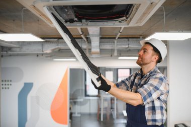 Güvenlik kaskı ve eldiven takan Hvac teknisyeni modern ofis binasında kaset tipi klima tamir ediyordu.