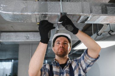 HVC teknisyenleri montaj sırasında havalandırma kanalında vidaları sıkıyor, koruyucu giysiler giyiyor ve uygun hava akışını sağlıyorlar.