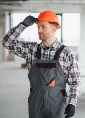 Turuncu bir miğferi ayarlayan inşaat işçisi, yoğun bir inşaat sahasında güvenlik ve profesyonelliğe odaklanmış vazifeler için hazırlanıyor.