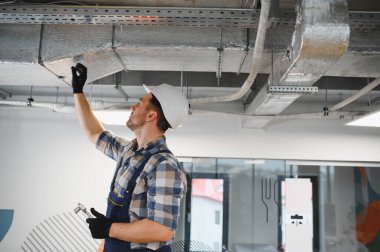 Hvac teknisyeni inşaat halindeki bir binada havalandırma sisteminin kurulumu sırasında metal hava kanallarını inceliyor.