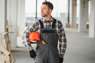 Kolunun altında turuncu bir miğfer tutan inşaat işçisi inşaat halindeki bir binanın sonraki adımlarını planlıyor.