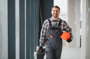 Gülümseyen hvac teknisyeni inşaat halindeki bir binada aletlerini ve miğferini taşıyor.