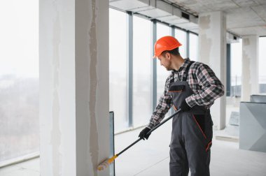 Boya silindiri kullanan profesyonel bir müteahhit, yenilenmekte olan bir binanın duvarlarına yeni bir kat boya sürüyor, iç mimari çalışmaların nasıl sonuçlandığını gösteriyor.