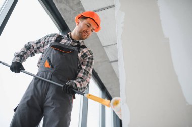 Boya silindiri kullanan profesyonel bir müteahhit, yenilenmekte olan bir binanın duvarlarına yeni bir kat boya sürüyor, iç mimari çalışmaların nasıl sonuçlandığını gösteriyor.