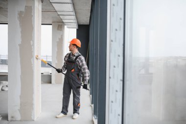 İnşaat işçisi koruyucu giysi ve miğfer takıyor. İnşaat onarımı sırasında boya silindiriyle duvarları boyuyor.