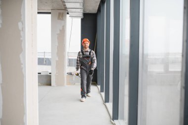 İnşaat işçisi üniforma giyiyor ve bina tadilatı sırasında bitmemiş binalarda yürüyor.