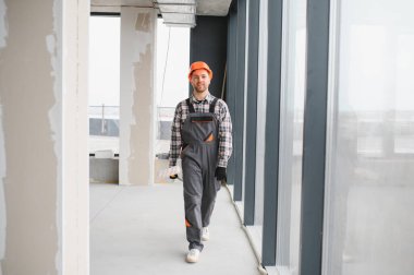 İnşaat işçisi inşaat halindeki bir binanın içinden güvenle geçiyor, aletlerle donatılmış ve güvenlik kaskı ve üniforması giyiyor.