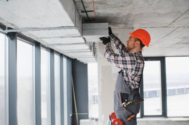 Turuncu kasklı bir inşaatçı inşaat halindeki bir binaya havalandırma sistemi kuruyor.