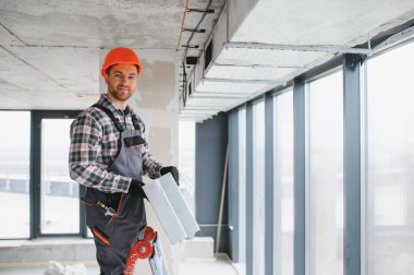 İnşaat işçisi, güvenlik kaskı ile modern bir binaya havalandırma kuruyor.