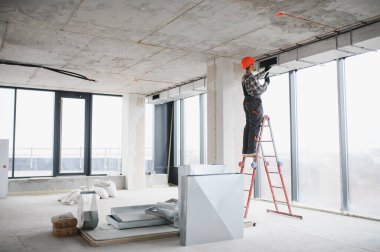 İnşaat işçisi merdivene tırmanıyor, bitmemiş bir binaya havalandırma sistemi kuruyor, uygun hava akışını ve verimliliği sağlıyor.