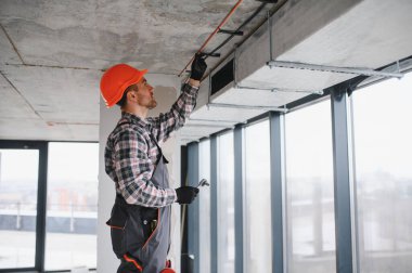 İnşaat işçisi koruyucu iş giysisi ve kask giyiyor, inşaat halindeki bir binaya havalandırma ve havalandırma sistemi kuruyor.