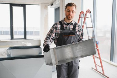Hvac teknisyeni inşaat halindeki bir binaya metal bir kanal parçası tutarak havalandırma sistemi kuruyor.