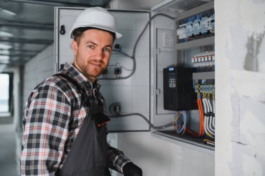 Güvenlik kaskı takan elektrikçi inşaat halindeki elektrik kontrol panelini kontrol ediyor.