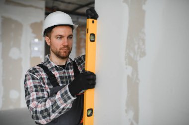 Bir yenileme projesi sırasında bir inşaat sahasında çalışırken alçıpanın dikeyliğini sağlamak için ruh seviyesini kullanan inşaatçı