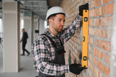 İnşaat sırasında bir tuğla duvarın dikey hizalanmasını sağlamak için ruh seviyesini kullanan inşaatçı, hassasiyet ve kaliteyi vurguladı