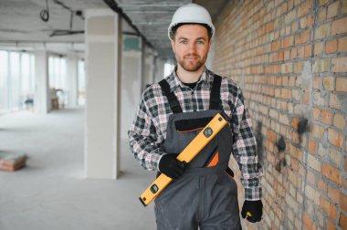 Bir miğfer takan ve ruhsal bir seviyede tutan inşaatçı inşaat halindeki modern bir binanın duvarlarını inceliyor.