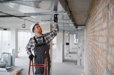 İnşaatçı inşaat sahasına havalandırma sistemi kuruyor, tadilat altındaki bir binanın havalandırması üzerinde çalışıyor.