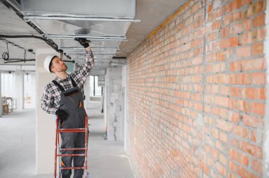 İnşaatçı merdiven üzerinde duruyor ve inşaat halindeki bir binaya klima sistemi kuruyor.