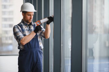 İnşaat işçisi, bina tadilatı sırasında pencere çerçevesine dolgu macunu sürüyor.