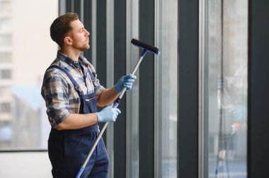 Bir ofis binasının camlarını temizleyen erkek işçi, en uygun hijyen ve güvenlik için eldiven giyerken teleskopik cam koruyucu kullanıyor.