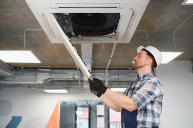 Hvac teknisyeni bir binanın içinde kaset tipi klima tamir ediyor. Güvenlik için başlık ve eldiven takıyor.