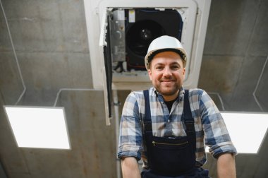 Havalandırma ve havalandırma sistemi üzerinde çalışırken güvenlik kaskı takan HVC teknisyeni gülümsüyor.