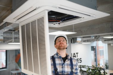 Hvac teknisyeni, bakım sırasında tavana monte edilmiş kaset tipi klima kontrolü yapıyor.