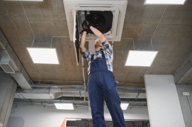 Hvac teknisyeni kaset tipi klima tamir ediyor. Güvenlik kaskı takıyor ve havalandırmayı ve soğutmayı sağlıyor.