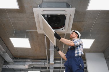 Güvenlik kaskı ve eldiven takan HVC teknisyeni bakım sırasında havalandırma filtresi kontrol ediyor.