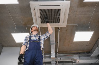 Güvenlik kaskı takan HVC teknisyeni ve bakım işleri sırasında havalandırma ünitesini denetliyor.