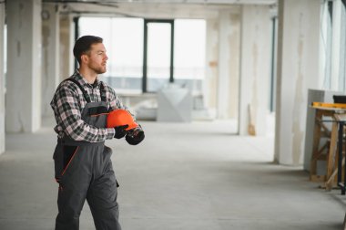 İnşaat işçisi inşaat halindeki bir binada turuncu bir kask tutuyor.