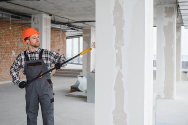 Boya silindiri kullanan profesyonel bir müteahhit, yenilenmekte olan bir binanın duvarlarına yeni bir kat boya sürüyor, iç mimari çalışmaların nasıl sonuçlandığını gösteriyor.
