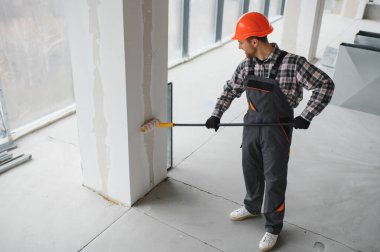 Boya silindiri kullanan profesyonel bir müteahhit, yenilenmekte olan bir binanın duvarlarına yeni bir kat boya sürüyor, iç mimari çalışmaların nasıl sonuçlandığını gösteriyor.