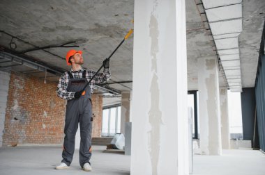 Boya silindiri kullanan profesyonel bir müteahhit, yenilenmekte olan bir binanın duvarlarına yeni bir kat boya sürüyor, iç mimari çalışmaların nasıl sonuçlandığını gösteriyor.