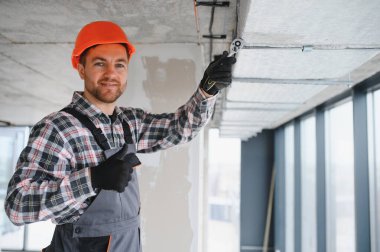 Tulum ve şapka giyen inşaatçı inşaat halindeki bir binanın havalandırma borularını sıkılaştırmak ve onay vermek için kilit anahtarı kullanıyor.