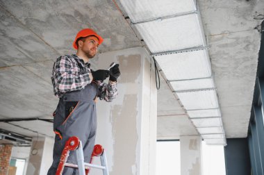 İnşaat işçisi merdivene havalandırma sistemi kuruyor, inşaat halindeki binanın havalandırması üzerinde çalışıyor.