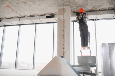 İnşaat işçisi, tamamlanmamış bir binaya havalandırma sistemi kurarken merdivene tırmanıyor. Bölgeye güvenlik ve verimlilik sağlıyor.