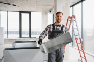 Hvac teknisyeni inşaat halindeki bir binada havalandırma sistemi kurulumu için metal havalandırma kanalı taşıyor.