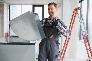 Hvac teknisyeni inşaat veya yenileme sırasında metal bir havalandırma borusu kuruyor, işaret veriyor.