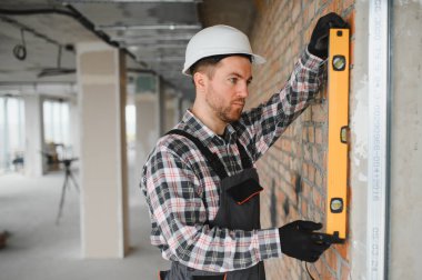 İnşaat sırasında tuğla duvarın dikey hizalanmasını sağlamak için ruh seviyesini kullanan inşaatçı