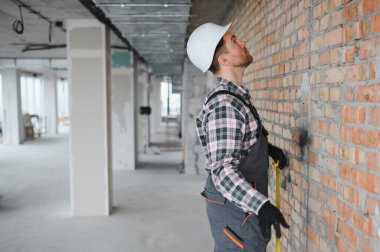 İnşaat işçisi inşaat halindeki tuğla duvarı incelerken mezura takıyor.