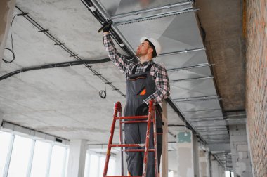 Güvenlik miğferi olan bir inşaatçı inşaat halindeki bir binanın merdivenine havalandırma boruları yerleştiriyor.