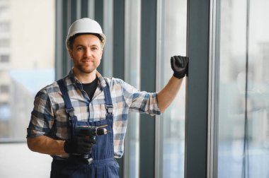 Modern ofis binasına güvenlik kaskı takan ve kablosuz matkap takan inşaat işçisi