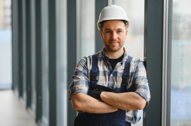 Kendine güvenen hvac teknisyeni sıkı bir şapka ve tulum giyiyor, modern bir binada kolları çaprazlanmış şekilde gülümsüyor, havalandırma ve havalandırma konusunda profesyonellik ve uzmanlık gösteriyor.