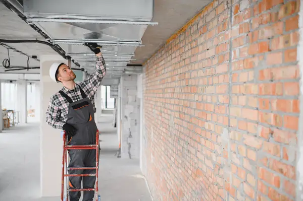 İnşaatçı merdiven üzerinde duruyor ve inşaat halindeki bir binaya klima sistemi kuruyor.