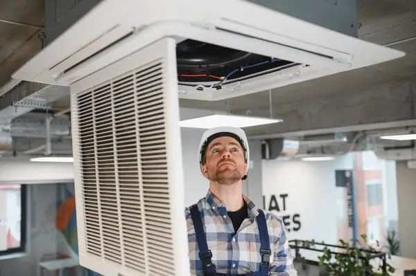 Hvac teknisyeni, bakım sırasında tavana monte edilmiş kaset tipi klima kontrolü yapıyor.