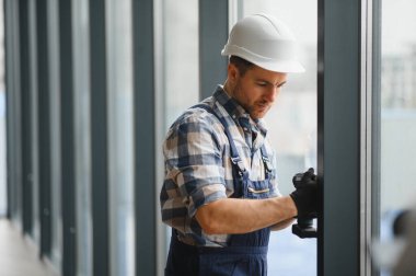 Modern binaya pencereler yerleştirilirken güvenlik kaskı takan ve kablosuz tornavida kullanan inşaat işçisi